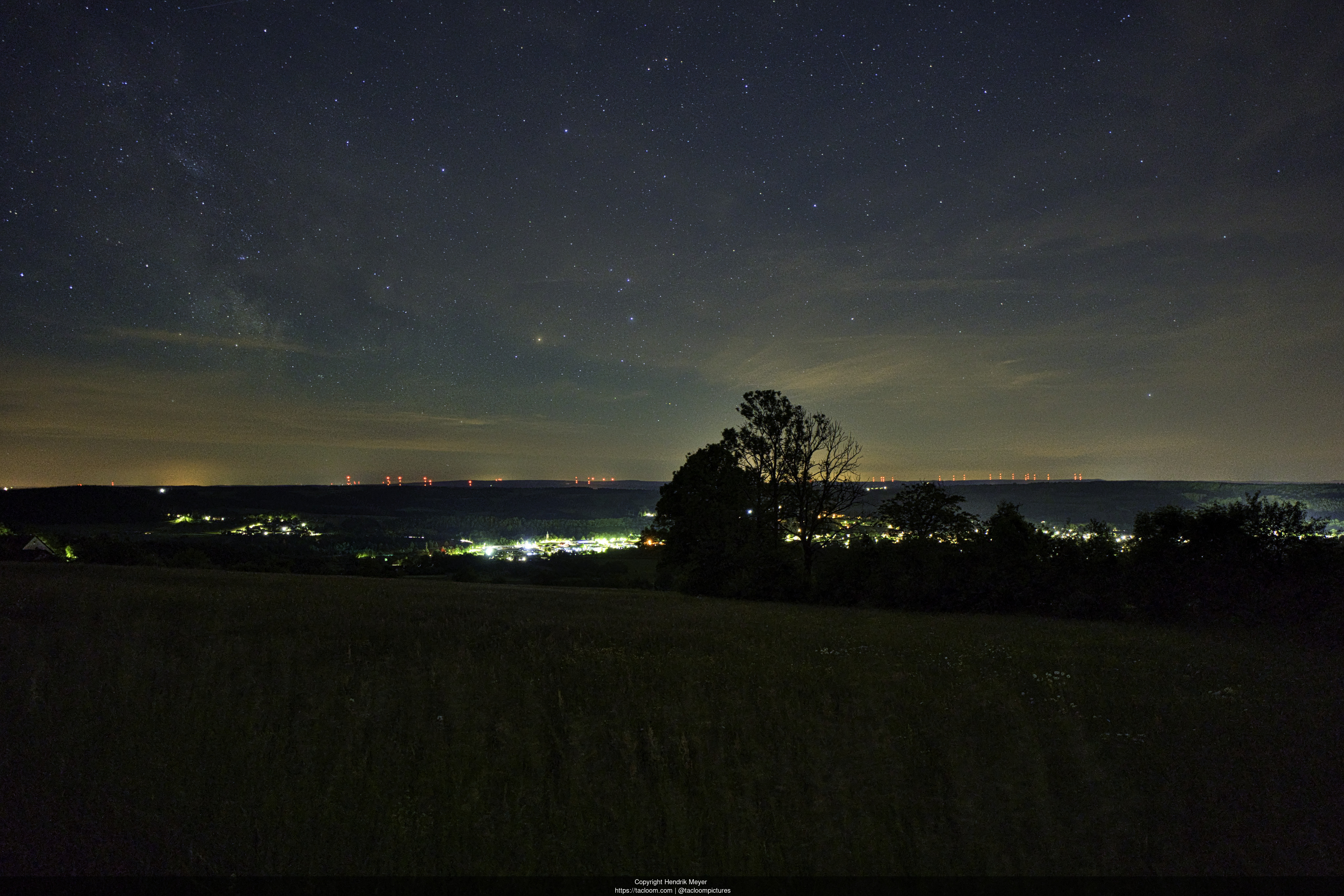 A clear sky with visible stars with a small city below. A field is visible in the front.